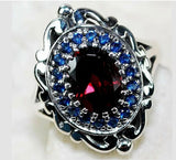 “Secrets of His Promises” Stunning four carat genuine Mozambique fire Garnet surrounded by lab blue sapphires set in solid ornate sterling silver.
